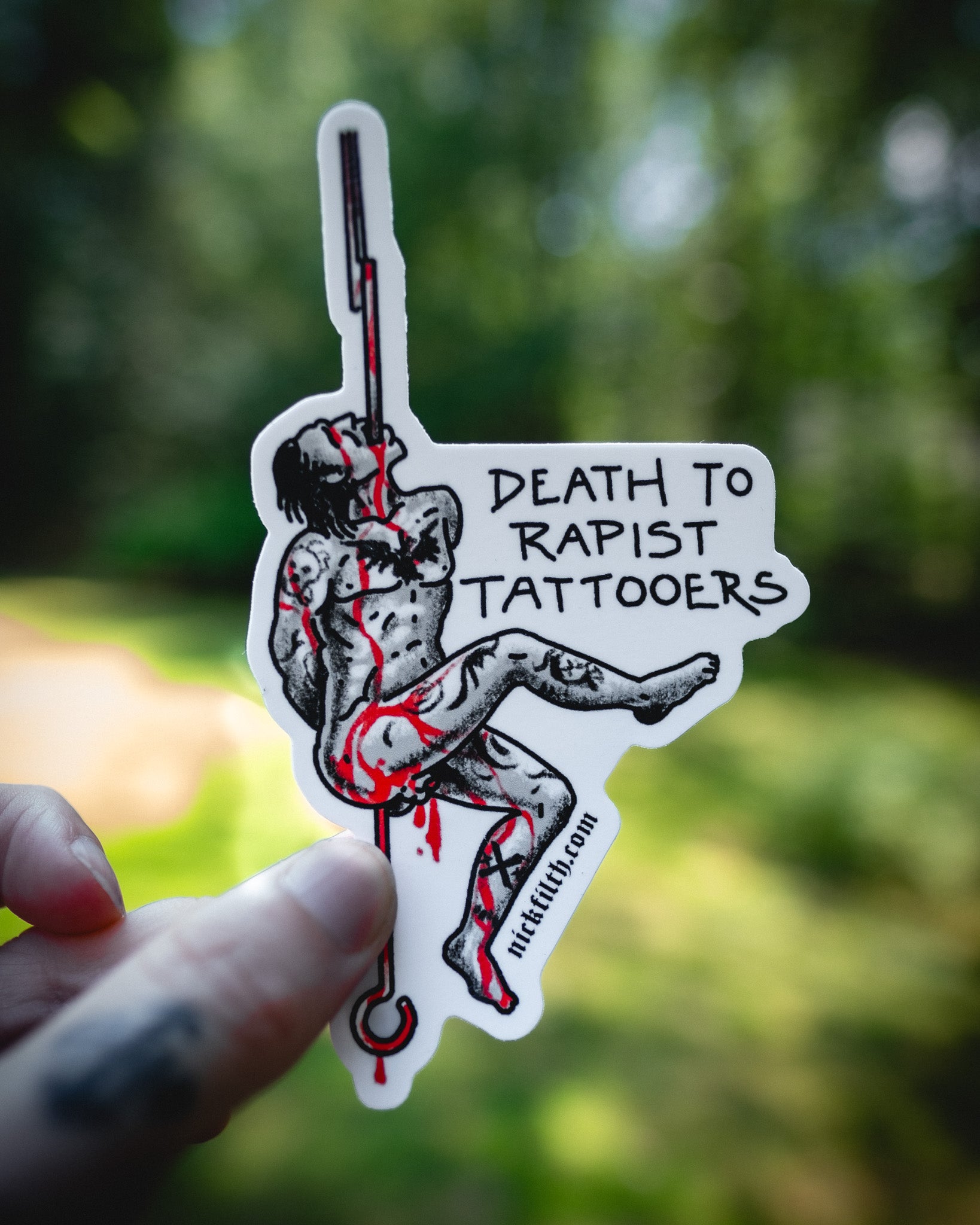 Sticker with graphic design and text held by a hand against a blurred natural background