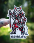 Sticker of a warrior cat with armor and a sword, held against a blurred green background.