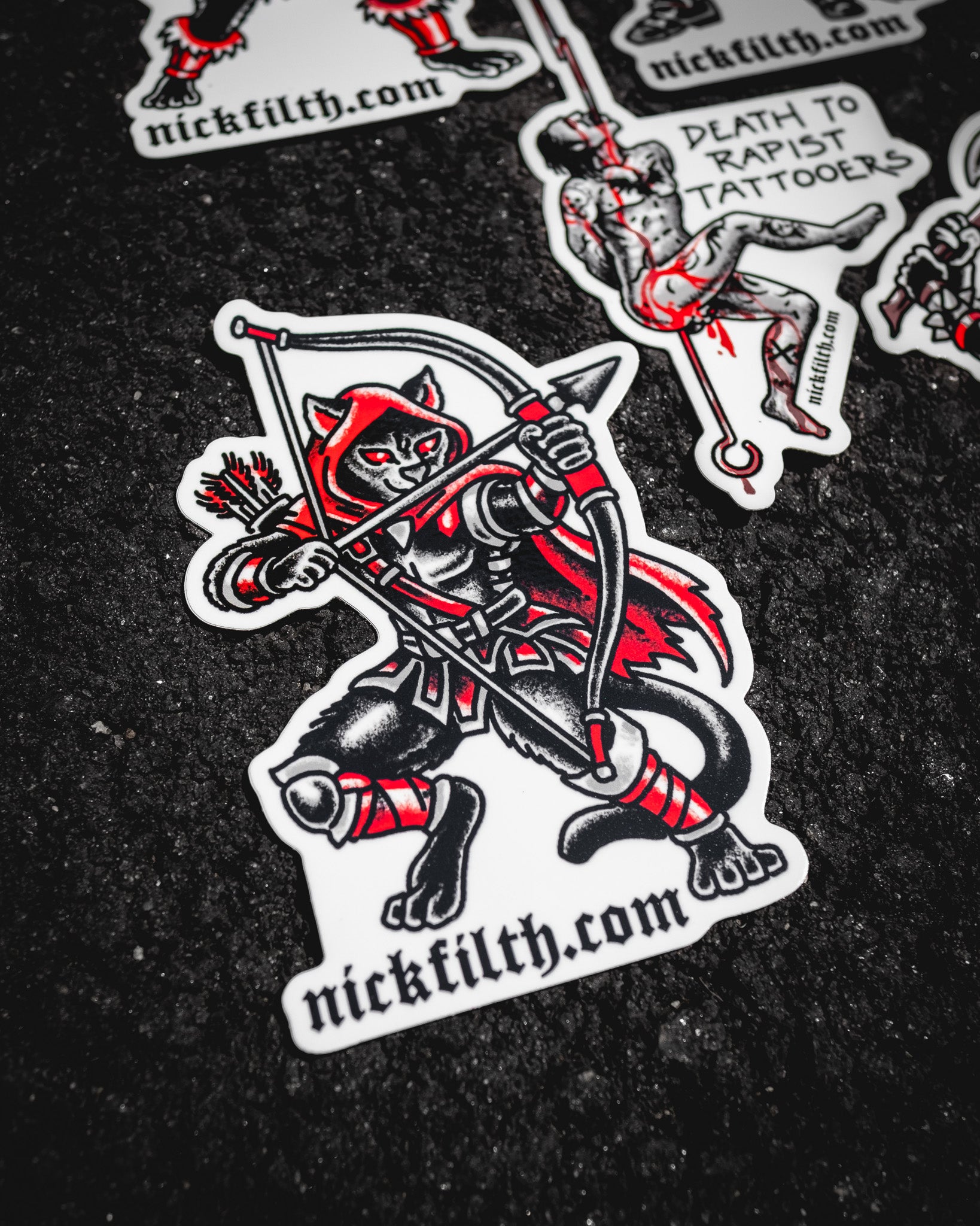 Sticker of a cat with a bow and arrow on a dark surface, featuring 'nickfilth.com'.