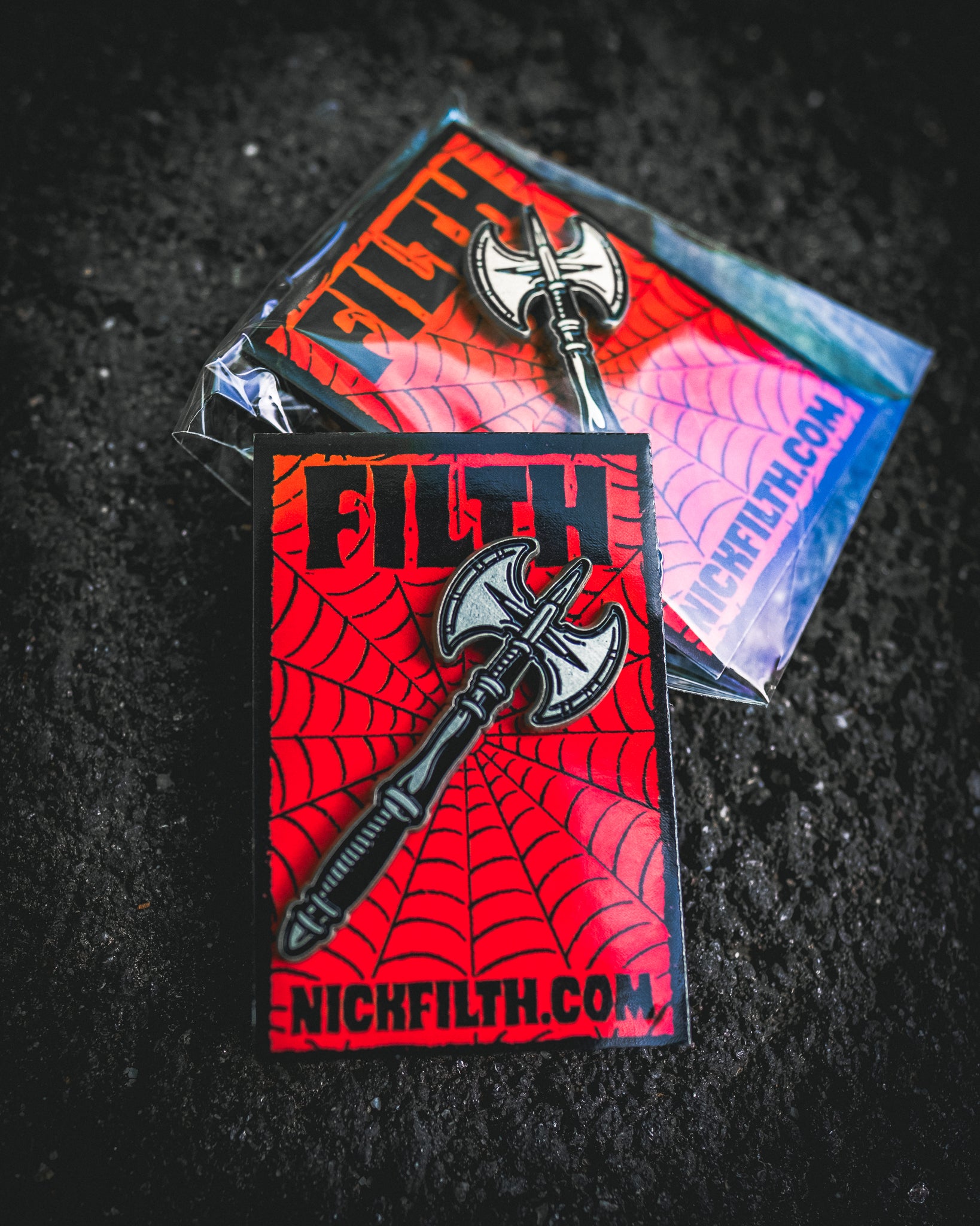 Pin with ax design on a red background, featuring 'NICKFILTH.COM' text, on a dark textured surface.