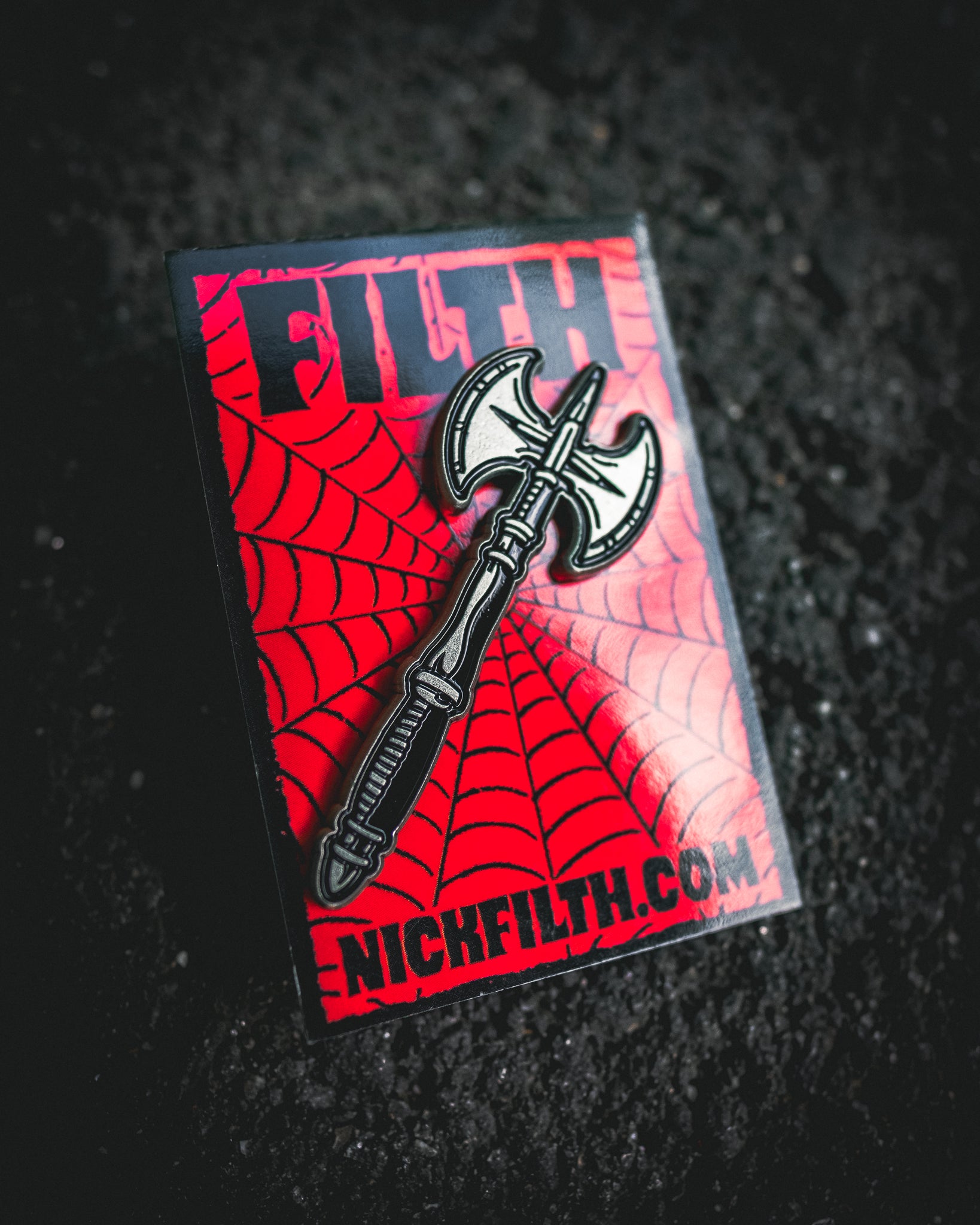 Pin with ax design on a red and black spider web background, featuring 'NICKFILTH.COM'