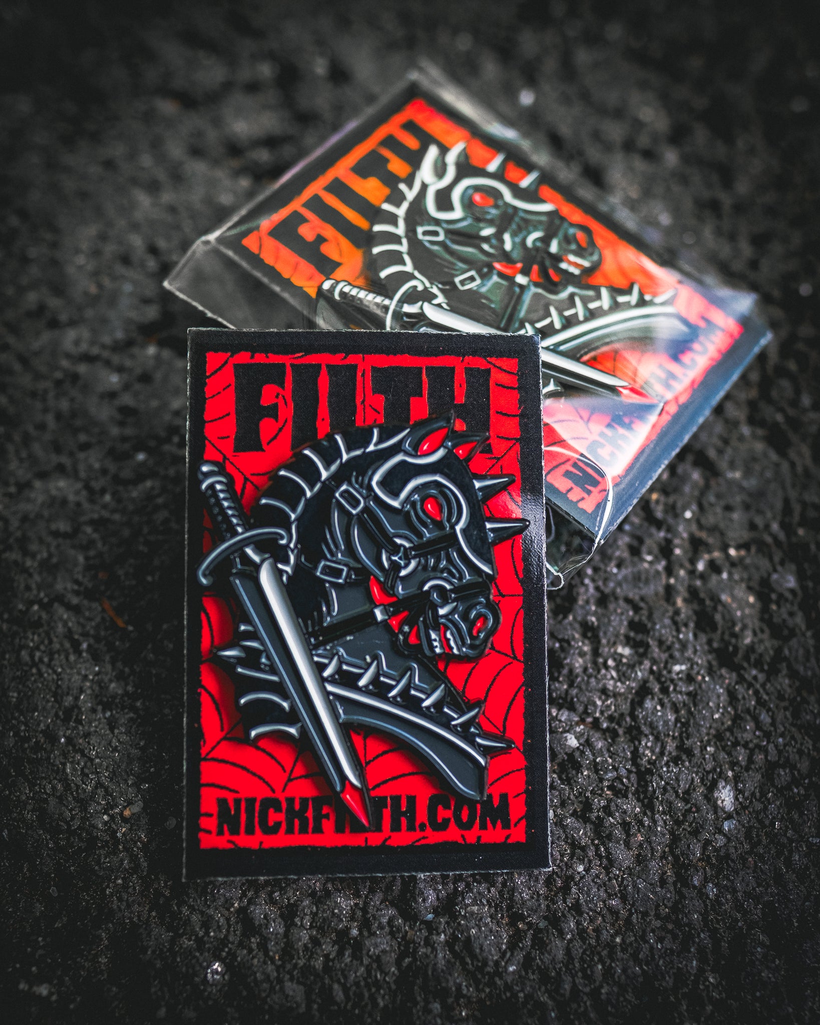Two black and red pins with a Horse and sword design on a dark textured background.