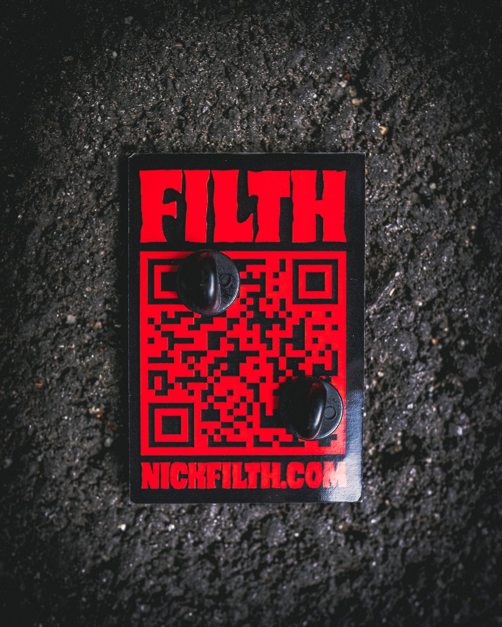 Black and red card with 'Filth' and a QR code on a textured black surface