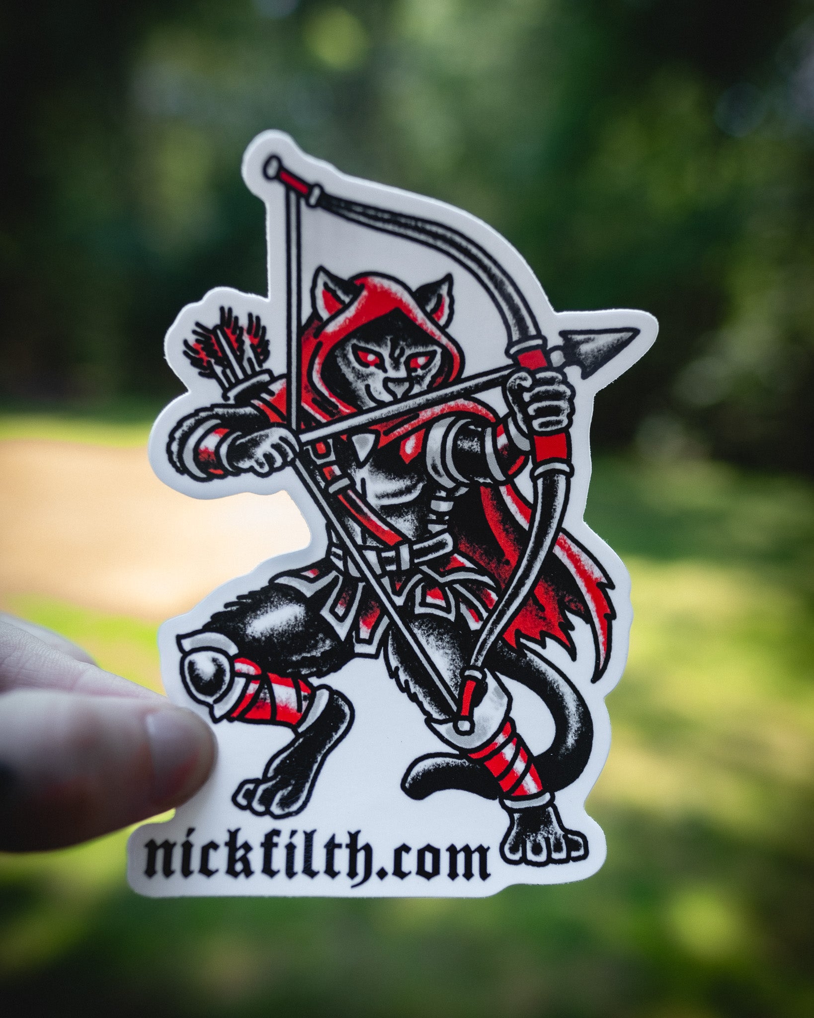 Sticker of a hooded figure with a bow and arrow held by a hand, against a blurred natural background.